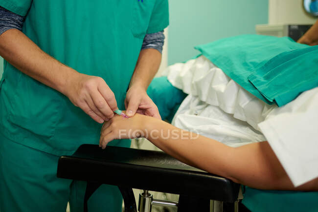 Урожай невизначених медичних помічників, що вставляють внутрішньовенний катетер в руку анонімному пацієнту, який лежить на дивані в операційній кімнаті — стокове фото