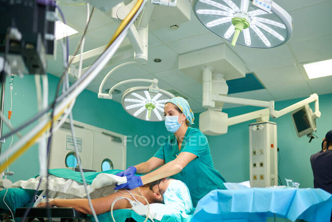 Low angle of anonymous concentrated female nurse in uniform and mask covering unrecognizable patient with sterile blanket before surgery in modern hospital — Stock Photo