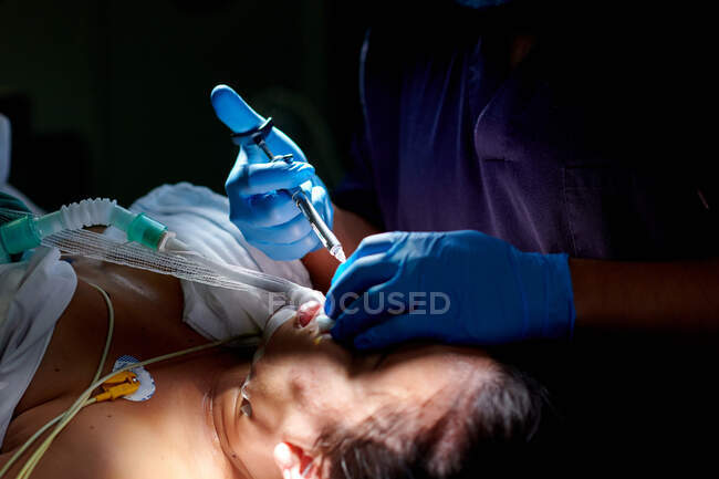 Cirujano anónimo de cultivo en uniforme médico y guantes que hacen la inyección con jeringa mientras realiza la operación de rinoplastia para el paciente femenino - foto de stock