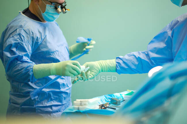 Бічний погляд на урожаю анонімних лікарів у хірургічних сукнях і масках, які допомагають один одному під час операції в сучасній лікарні. — стокове фото
