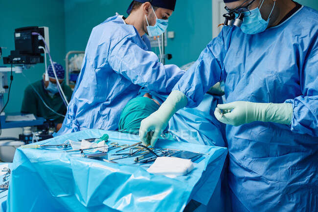 Анонімні фокусувалися на чоловічому хірургу в синій масці сукні і збільшенні окулярів, що стоять біля стерильного поля з різними медичними інструментами під час роботи в сучасній клініці. — стокове фото
