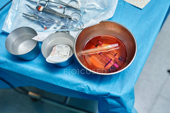 Сверху шприцы в миске с окровавленной водой, помещенной на стерильное поле рядом с различными хирургическими инструментами в операционной — стоковое фото
