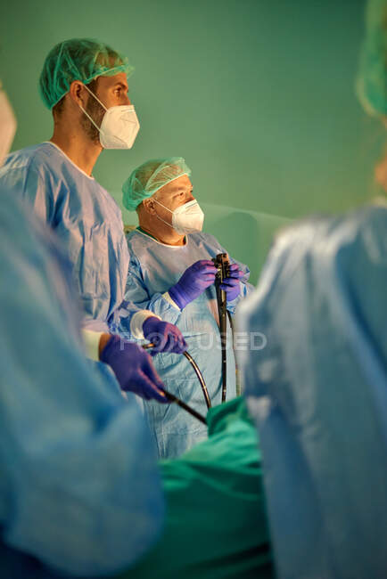 Gruppe anonymer Ärzte in Operationskleidung und Masken blickt auf Monitor, während sie den Patienten mit Endoskop vor der Operation in einer modernen Klinik untersucht — Stockfoto