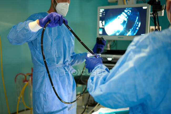 Crop unrecognizable doctor in surgical gown and mask dipping endoscope into water while preparing for procedure with colleague in operating room — Stock Photo