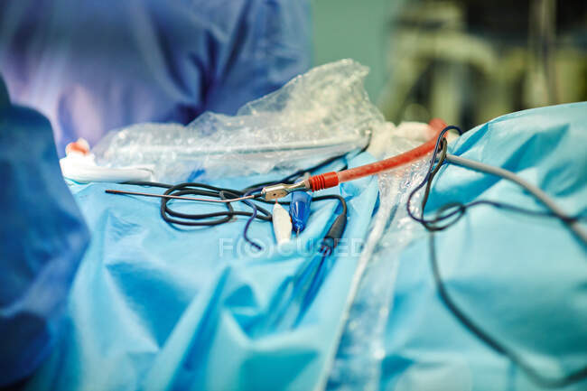 Médicos irreconocibles de cultivo de pie cerca de la mesa de operaciones con catéteres de succión de sangre y agujas durante la cirugía en la clínica moderna - foto de stock