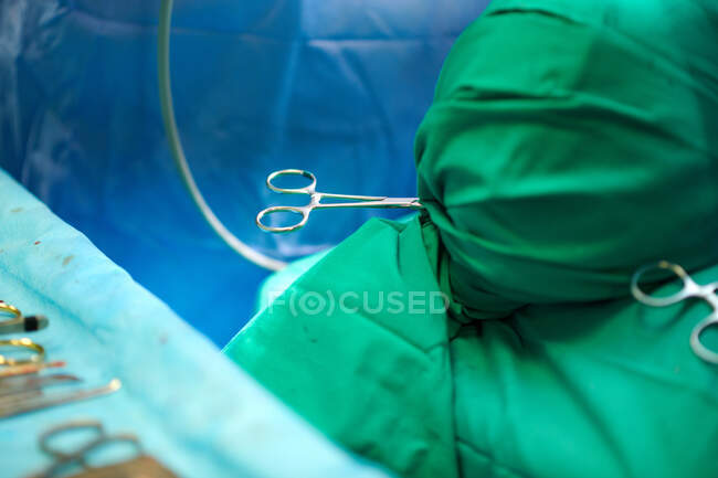 From above of crop unrecognizable patient with head wrapped in sterile cloth lying on operating table during surgery in hospital - foto de stock