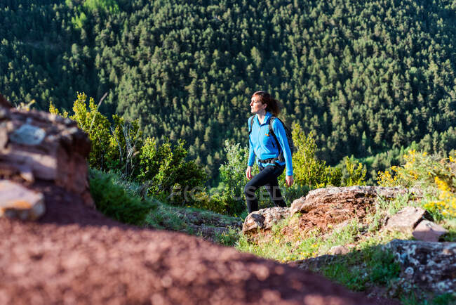 Traveling female with backpack trekking in rocky terrain in mountains on sunny day and looking away — Foto stock