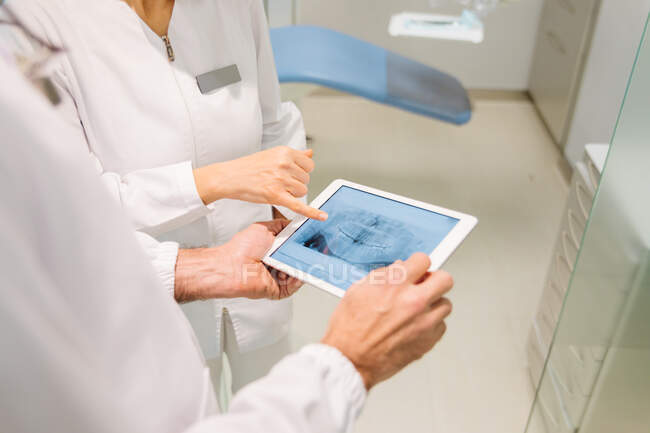 Из выше урожая анонимных стоматологов в медицинских халатах обследование состояния зубов на рентгеновском снимке на таблетках во время совместной работы в современной стоматологической клинике — стоковое фото
