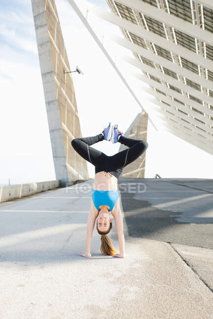 Full body content fit sportswoman in activewear performing handstand with feet together on sunny street - foto de stock