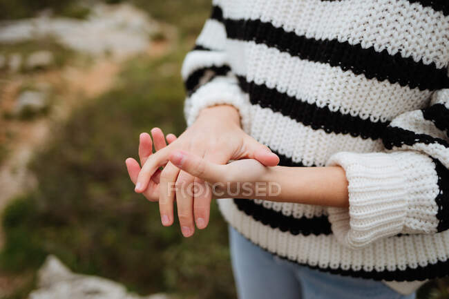 Crop anonymous female tourist in knitted sweater with ornament showing friendship gesture on mountain in daylight - foto de stock
