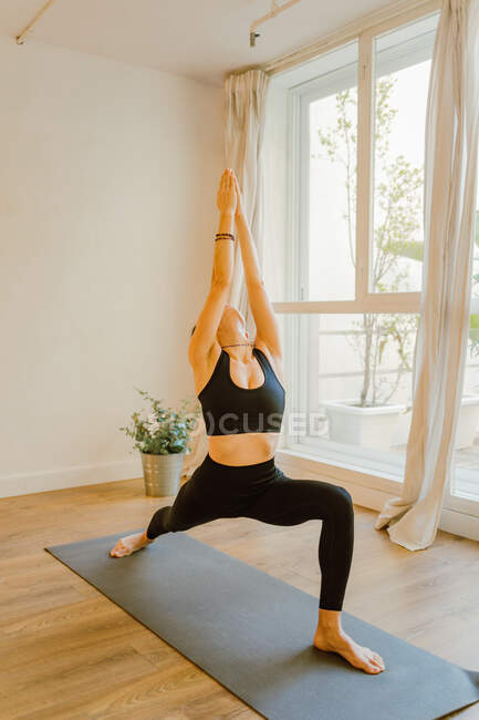 Junge flexible Frau in Sportkleidung steht in Trikonasana-Pose, während sie Yoga mit erhobenem Arm praktiziert und im Haus nach oben schaut — Stockfoto