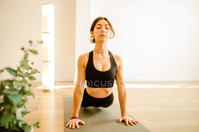 Femelle flexible méconnaissable en vêtements de sport montrant la pose du bhujangasana tout en pratiquant le yoga dans la pièce de la maison en plein jour — Photo de stock