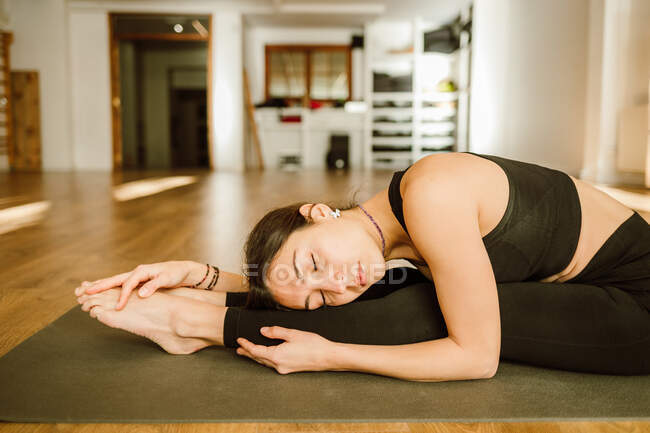 Young mindful female in sportswear leaning forward while stretching back with closed eyes at home — Fotografia de Stock