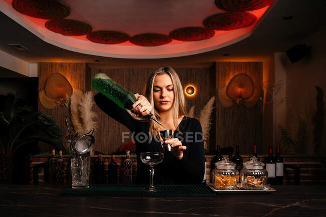 Задоволення молодої жінки барменом з довгим світлим волоссям, що готує алкоголь, п'є коктейль за стійкою — стокове фото