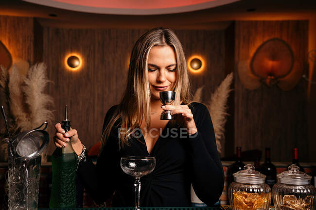 Задоволення молодої жінки барменом з довгим світлим волоссям, що пахне алкоголем, готуючи коктейль за стійкою — стокове фото
