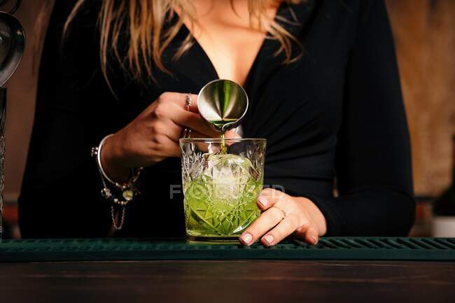Culture femme barman méconnaissable poring liqueur verte dans le verre avec des glaçons tout en préparant un cocktail alcoolisé dans le restaurant — Photo de stock