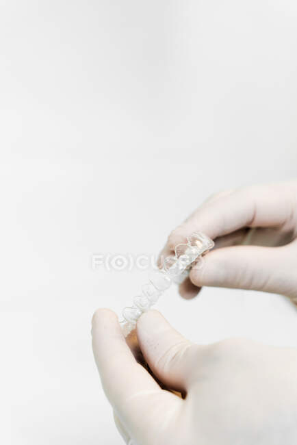 Урожай неузнаваемый дантист в латексных перчатках держа шину на белом фоне в стоматологической клинике — стоковое фото