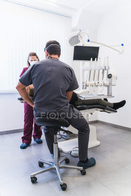 Dentista irreconhecível em uniforme examinando pacientes dentes perto de enfermeira na moderna clínica odontológica equipada — Fotografia de Stock