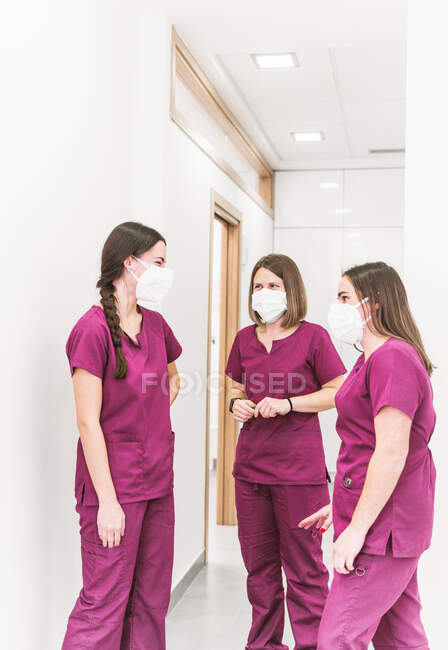 Група молодих медичних сестер у медичній формі та маски, що розмовляють у сучасному лікарняному коридорі — стокове фото