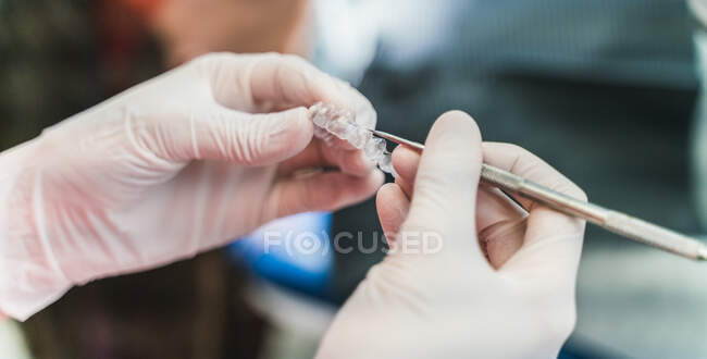 Crop unrecognizable dentist in latex gloves holding ultra thin veneers and scaler while working in dental clinic — Stock Photo