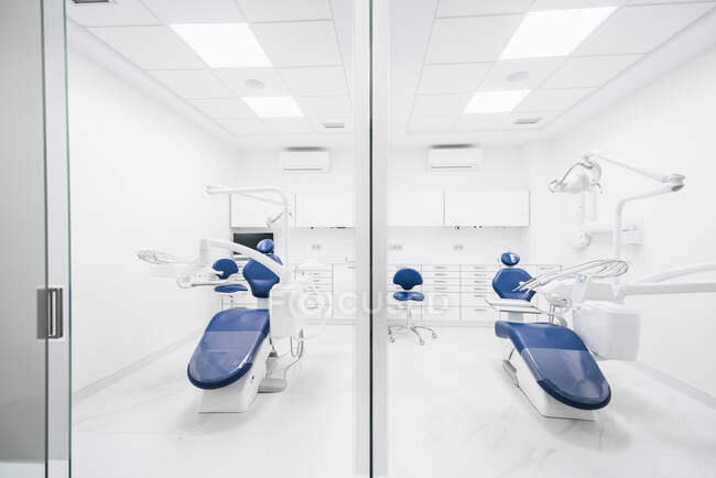 Внутрішня частина сучасної акуратної стоматологічної клініки з синім кріслом і білими меблями, оснащеними сучасною стоматологічною машиною і інструментами. — стокове фото