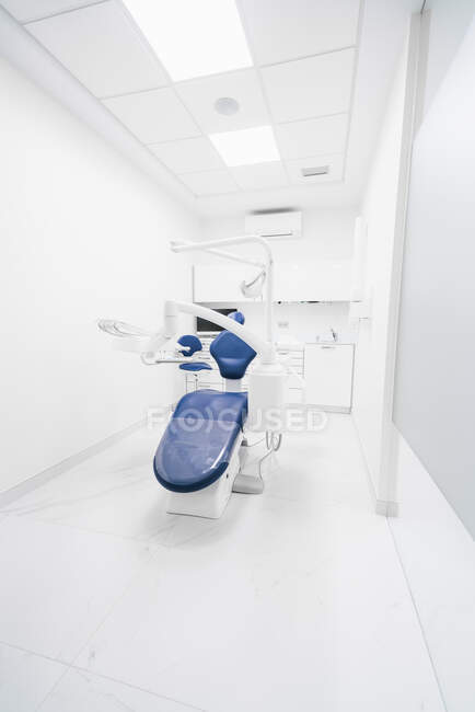 Intérieur de clinique dentaire contemporaine bien rangée avec chaise bleue et mobilier blanc équipé d'une machine dentaire moderne et d'instruments — Photo de stock