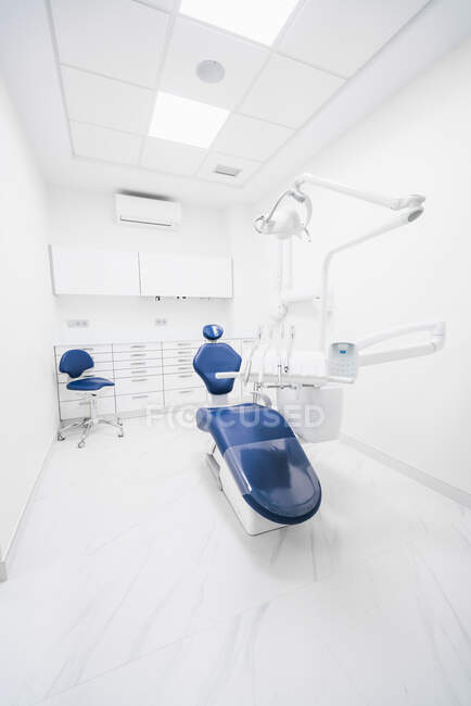 Interieur einer modernen, aufgeräumten Zahnklinik mit blauem Stuhl und weißen Möbeln, ausgestattet mit moderner Zahnmaschine und Instrumenten — Stockfoto
