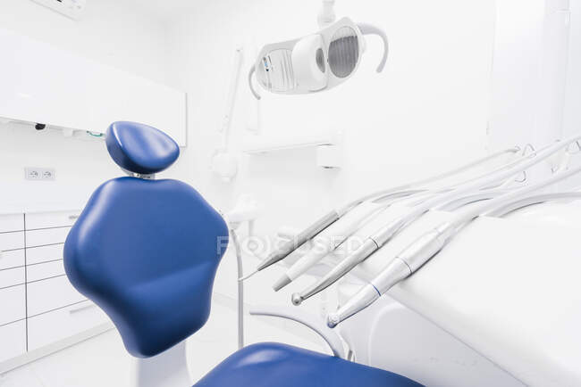 Интерьер опрятной легкой стоматологической клиники с синим стулом и современным тренажером — стоковое фото