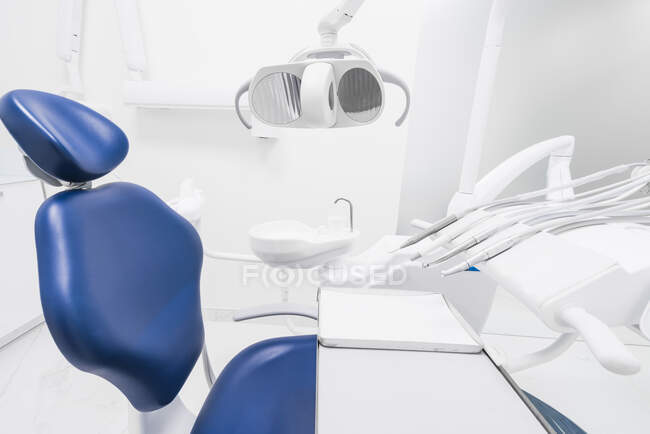 Intérieur de la clinique dentaire claire rangée avec chaise bleue et appareil de forage moderne — Photo de stock