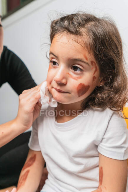 Mother with tissue wiping adorable little daughters face covered with body art paints — Stock Photo
