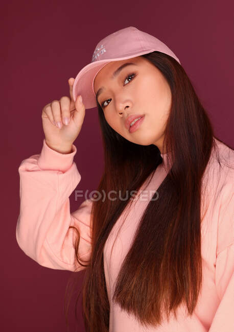 Portrait de jeune femme asiatique sérieuse en studio portant des vêtements roses sur fond grenat — Photo de stock