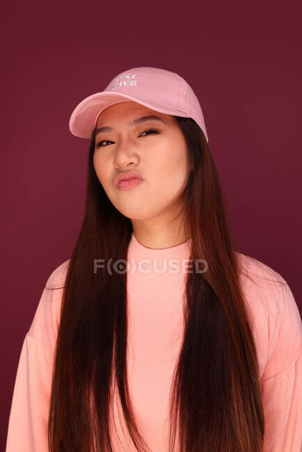 Portrait de jeune femme asiatique heureuse en studio portant des vêtements roses sur fond grenat — Photo de stock