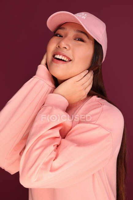 Портрет счастливой молодой азиатки в студии в розовой одежде на фоне граната — стоковое фото