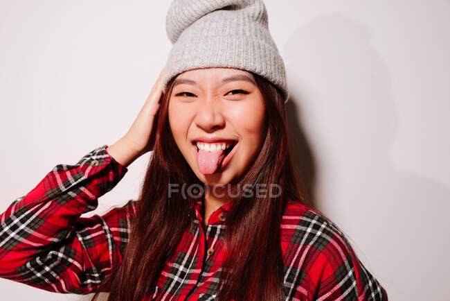 Primer plano retrato de alegre asiática joven sobresaliendo lengua y mirando a la cámara - foto de stock