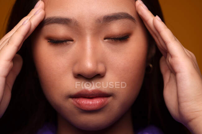 Mujer joven china preocupada con los ojos cerrados sobre fondo amarillo - foto de stock