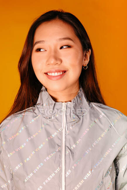 Retrato de una joven asiática con expresión seria. Lleva una chaqueta gris y mira hacia otro lado sobre un fondo amarillo. - foto de stock