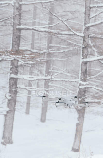 Современный белый беспилотник пролетает над снежной поляной в замерзших зимних лесах днем — стоковое фото