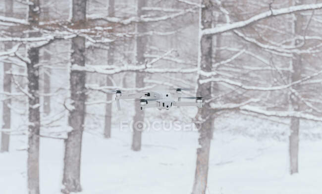 Современный белый беспилотник пролетает над снежной поляной в замерзших зимних лесах днем — стоковое фото