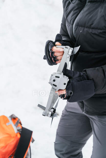 Cropped unrecognizable male in warm winter clothes and hood holding contemporary UAV in snowy freezing forest — Stock Photo