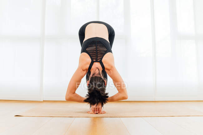 Cuerpo completo de hembra sin rostro meditando en Big Toe asana durante la práctica de yoga sobre alfombra deportiva en estudio - foto de stock
