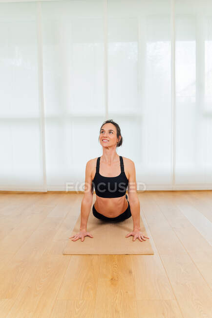 Visão frontal mulher alegre fazendo exercício Bhujangasana durante sessão de ioga em casa no tapete esportivo — Fotografia de Stock