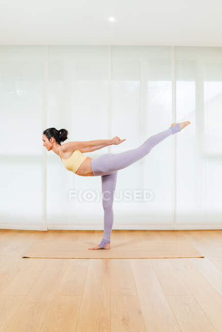 Visão lateral corpo inteiro de pernas de alongamento feminino enquanto se dobra para a frente e levantando a perna durante a aula de ioga mista — Fotografia de Stock