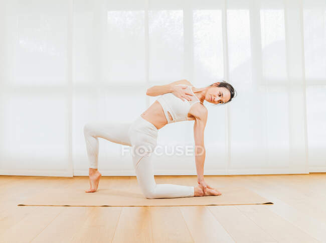 Visão lateral corpo inteiro de fêmea focada fazendo backbend com crescente lunge no joelho e pé tocante — Fotografia de Stock