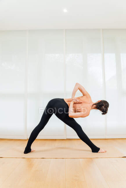 Vue du dos corps entier de femme torse nu méconnaissable dans les leggings noirs étirant les jambes et améliorant la flexibilité pendant la pratique du yoga — Photo de stock