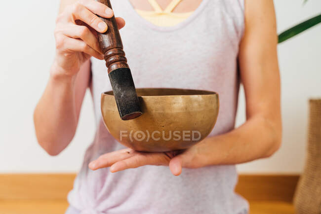 Cultivez une femme anonyme méditant avec un bol de chant tibétain en bronze pendant une séance de yoga en studio — Photo de stock