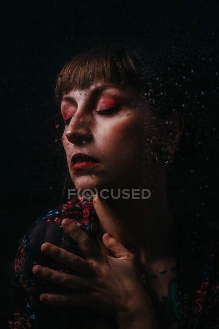 Crop upset female with closed eyes standing behind translucent glass with water droplets — Stock Photo