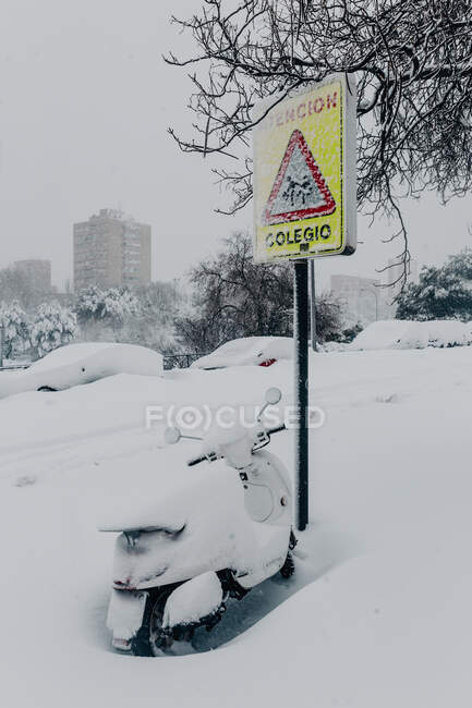 Contemporary motorbike parked near road sign and covered with thick layer of snow in city suburb on freezing winter day — Stock Photo
