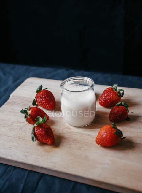 From above of transparent glass jar of milk near fresh sweet strawberries for smoothie on black background — Stock Photo