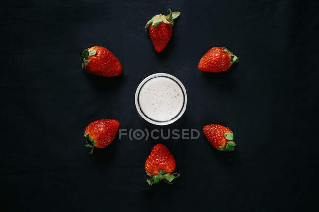 Du dessus de pot en verre transparent de lait près de fraises douces fraîches pour smoothie sur fond noir — Photo de stock