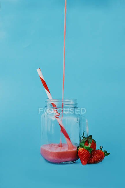 Glass jar with flow of tasty beverage with striped drinking tube near whole strawberries — Stock Photo